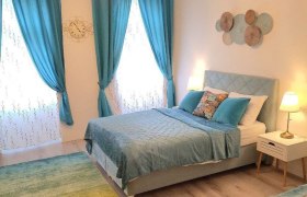 Family Apartments Neunkirchen, © UEK Immobilienverwaltungs GmbH Ein gemütliches Schlafzimmer mit blauen Vorhängen, einem Doppelbett und dekorativen Kissen. Zwei Nachttischlampen beleuchten den Raum.