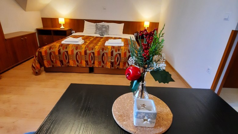 Doppelzimmer(c)Ildiko Davidne Nagy, © Ildiko Davidne Nagy Ein gemütliches Doppelzimmer mit einem dekorierten Tisch im Vordergrund und einem Bett im Hintergrund.