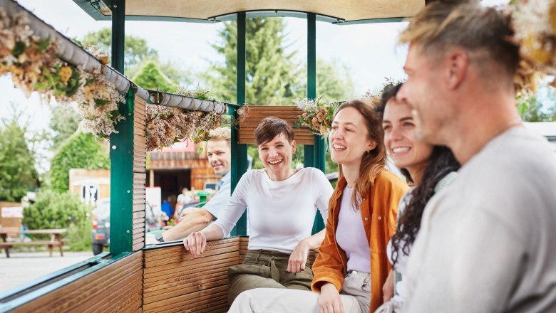 Mohnexpress, © © Waldviertel Tourismus, Gerhard Wasserbauer Eine Gruppe von Menschen sitzt lächelnd in einem offenen Wagen, der mit Blumen dekoriert ist.