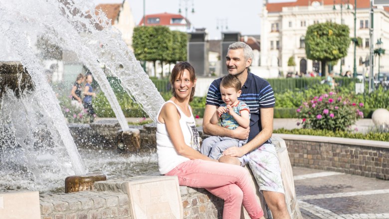 TDR-Hauptplatz Tulln, © Rrobert Herbst Eine Familie sitzt an einem Brunnen in einer Stadt mit historischen Gebäuden im Hintergrund.