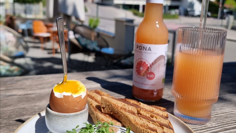 TDR-Statue EgontoGo-innen, © Yana Tereshchenko Toast, gekochtes Ei und Saft am Tisch im Aussenbereich