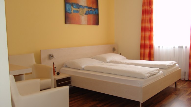 Kirchenwirt Jöch, © Kirchenwirt Jöch Ein modernes Hotelzimmer mit Doppelbett, gelben Wänden und einem abstrakten Gemälde.