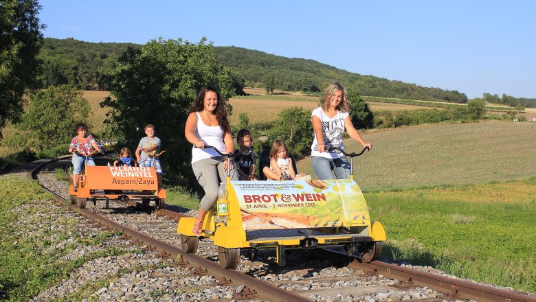Weinvierteldraisine, © Gemeinde Ernstbrunn Menschen fahren auf Draisinen durch eine ländliche Landschaft.
