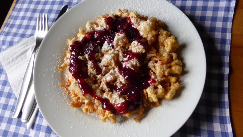 Waldburgangerhütte, © Maria Stroebl Ein Teller mit Kaiserschmarrn und roter Grütze auf einem blau-weiß karierten Tuch.