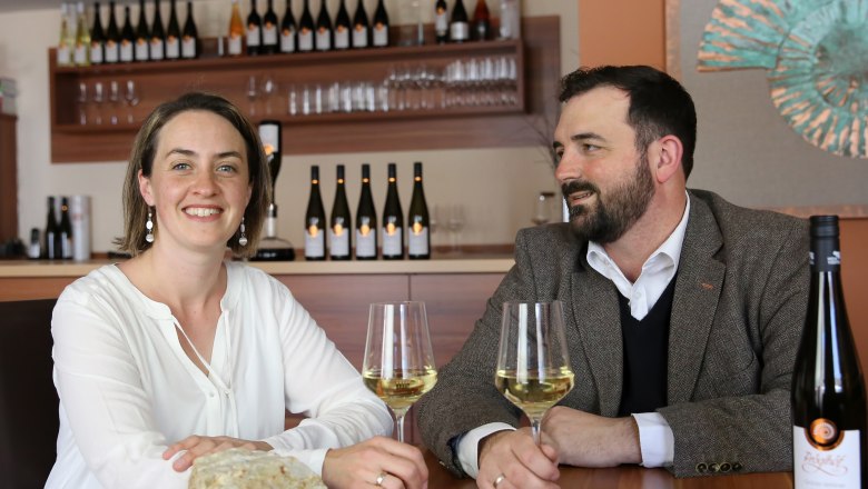 Marianne und Markus Pröglhöf, © Matthias Karasek Zwei Personen sitzen an einem Tisch mit Weingläsern und Weinflaschen im Hintergrund.