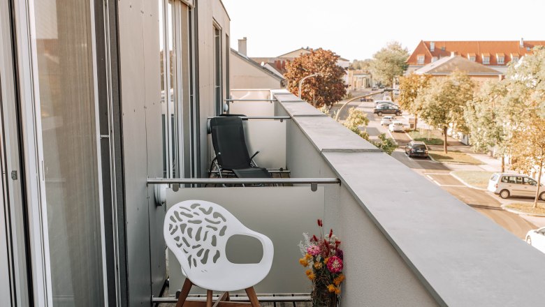 Business Terrasse HEINhotel vienna airport, © HEINhotel vienna airport Balkon mit weißem Stuhl und Blumenstrauß, Blick auf Straße und Gebäude.