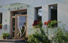 Wein + Bett Wiedeck, © Andrea Wiedeck Eingang eines Gebäudes mit der Aufschrift 'wein + bett', umgeben von Blumen.