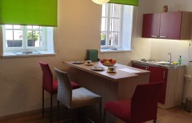 Küche, © Christian Naschitz Küche mit Esstisch, Stühlen und Fenster mit grünem Rollo.