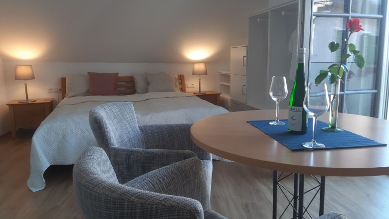 Apartment Smaragd, © Familie Heinzl Gemütliches Schlafzimmer mit Doppelbett, Tisch, zwei Stühlen, Weinflasche und Gläsern.