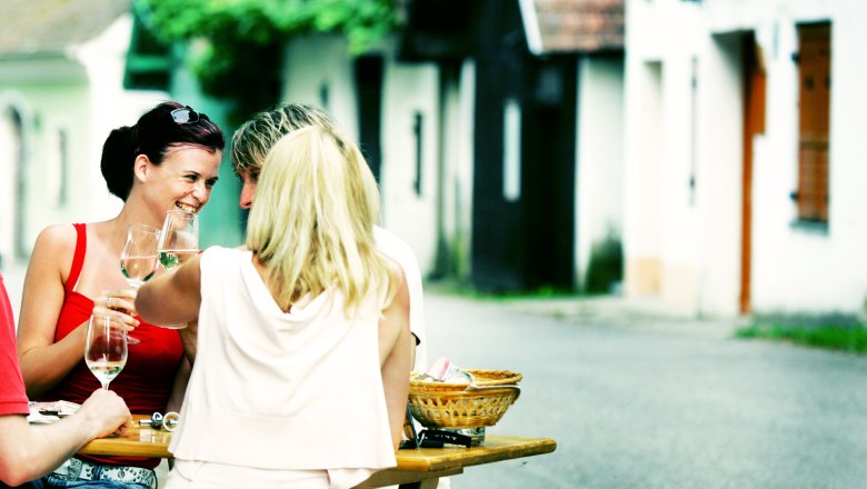 Ahrenberger Kellergasse, © Mostviertel Tourismus, weinfranz.at Menschen sitzen an einem Tisch in einer Kellergasse und trinken Wein.