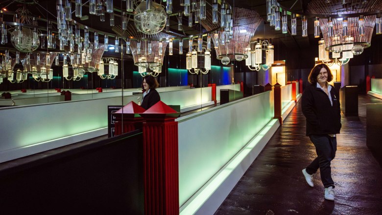 Steininger LOISIUM WeinWelt, © Pamela Schmatz Eine Person geht durch einen Raum mit futuristischer Beleuchtung und Spiegeln.