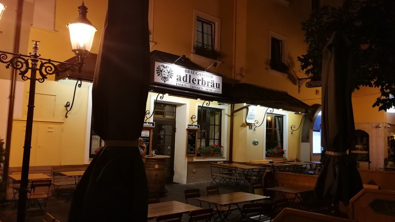 Adlerbräu Tulln, © Roman Zöchlinger Nachtaufnahme eines Restaurants mit dem Schild 'Adlerbräu' und leeren Tischen im Freien.