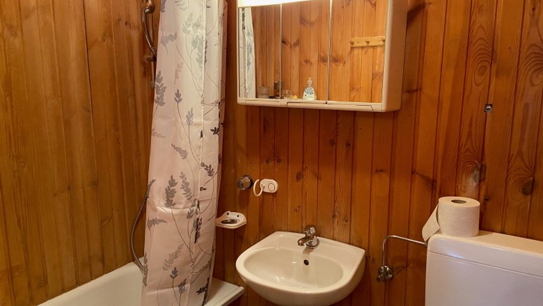 Badezimmer, © Wiener Alpen Holzvertäfeltes Badezimmer mit Badewanne, Duschvorhang, Waschbecken und Spiegelschrank.