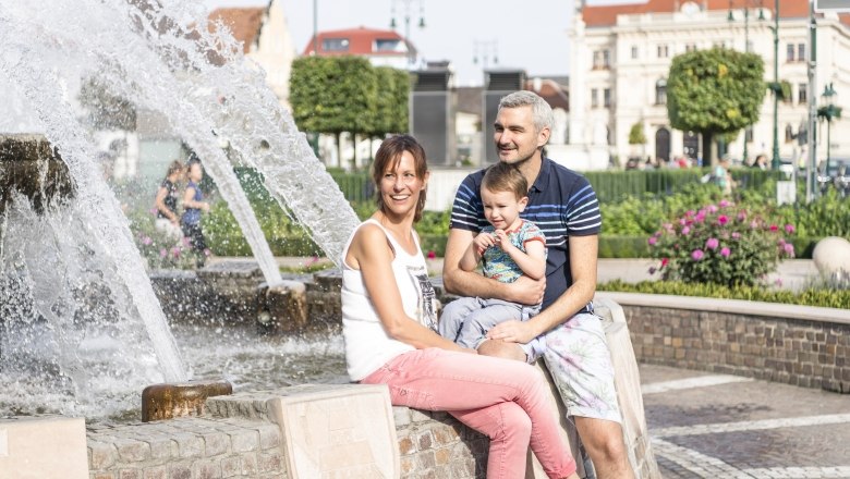Tullner Hauptplatz, © Stadtgemeinde Tulln/Robert Herbst Eine Familie sitzt lächelnd an einem Brunnen auf dem Tullner Hauptplatz.