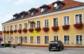 Außenansicht, © Gasthof Die kleine Post Gelbes Gebäude mit roten Blumen und Autos davor.