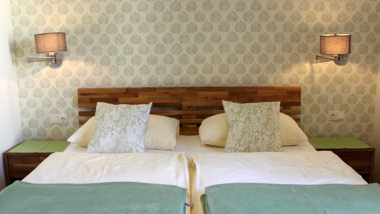 Gemütliche Zimmer, © Magdalena Donhauser Gemütliches Zimmer mit Doppelbett, Mustertapete, Wandlampen, Nachttischen und Kissen.