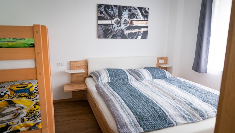 Schlafzimmer (Doppelbett + Stockbett), © Manuel Hahn Schlafzimmer mit Doppelbett, Etagenbett und Wandbild eines Autoteils.