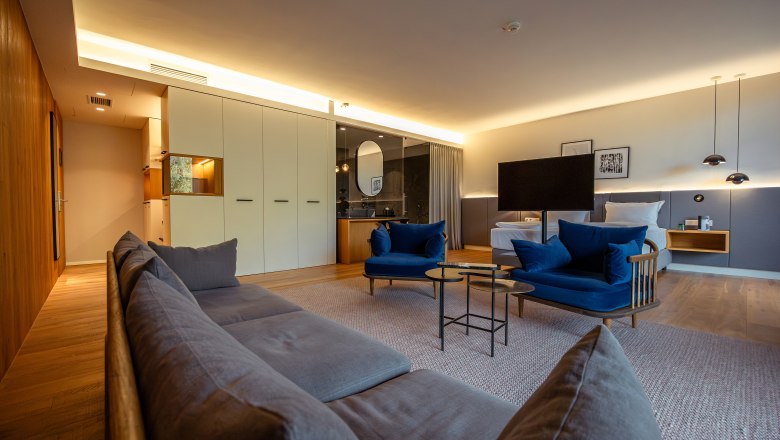 Steigenberger Hotel & Spa, Krems, © Niederösterreich Werbung/ Maximilian Pawlikowsky Modernes Hotelzimmer mit blauen Sesseln, grauem Sofa, großem Bett und stilvoller Beleuchtung.