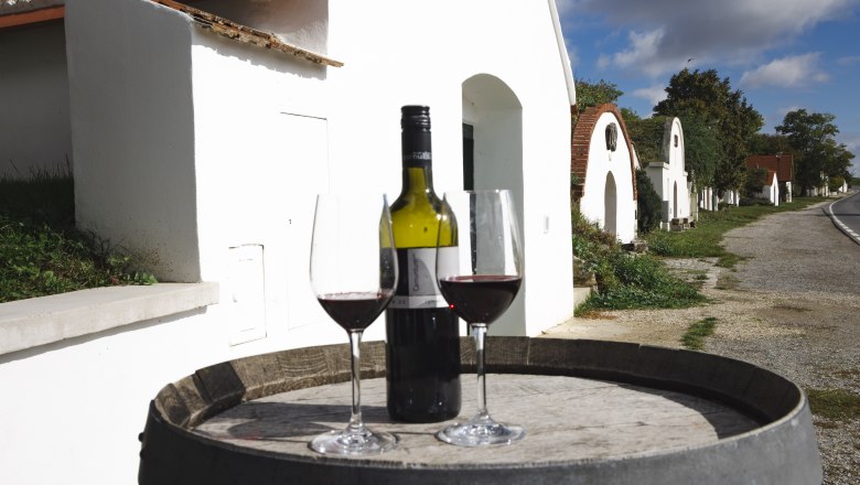 Kellergasse Prellenkirchen, © Donau Niederösterreich, Barbara Elser zwei Weingläser und eine Rotweinflasche auf einem Weinfass, im Hintergrund die Kellergasse