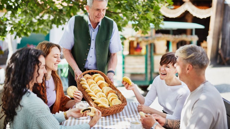 Mohnzelten beim Mohnwirt Neuwiesinger, © © Waldviertel Tourismus, Gerhard Wasserbauer Der Mohnwirt serviert einer Gruppe von vier Personen Mohnzelten an einem Tisch im Freien.