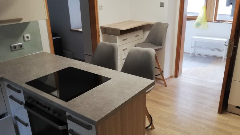 Küche, © Günter Lammer Moderne Küche mit Kochinsel, zwei grauen Stühlen und Holzfußboden.