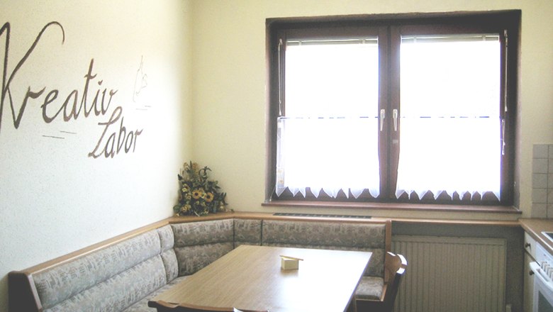 Esstisch in der Küche, © Anke Spreitzer Küche mit Eckbank, Tisch und Schriftzug 'Kreativ Labor' an der Wand.