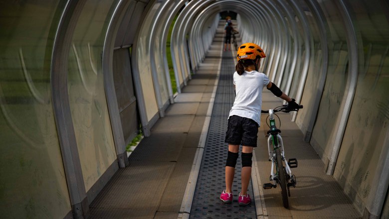 Förderband im Mini Bikepark, © Wexl Arena St. Corona am Wechsel Kind mit Fahrrad auf Förderband im überdachten Tunnel.