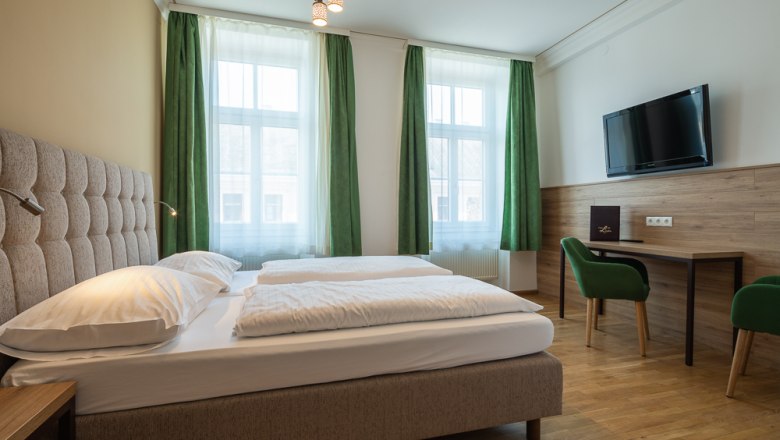 Hotel Unter den Linden 206, © Hotel Unter den Linden Hotelzimmer mit Doppelbett, grüne Vorhänge, Schreibtisch, Stuhl und Wand-TV.