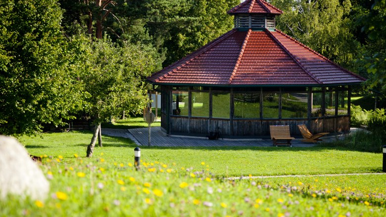 SoleAerium, © Stadtgemeinde Mank Ein Pavillon mit rotem Dach in einem grünen Park, umgeben von Bäumen und Blumen.