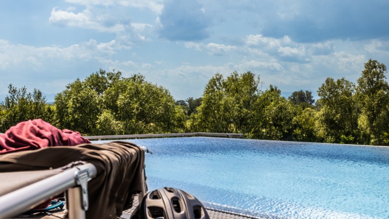Pool, © Wiener Alpen / Martin Fülöp Ein Infinity-Pool mit Bäumen im Hintergrund und einem Fahrradhelm im Vordergrund.