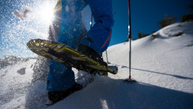 Schneeschuhwanderung, © Wiener Alpen/Claudia Ziegler Nahaufnahme eines Schneeschuhs im Schnee mit Sonnenlicht im Hintergrund.