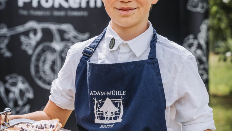 Kind serviert belegte Brote, © Monika Pölzer Ein Kind in einer blauen Schürze hält ein Tablett mit belegten Broten im Freien.