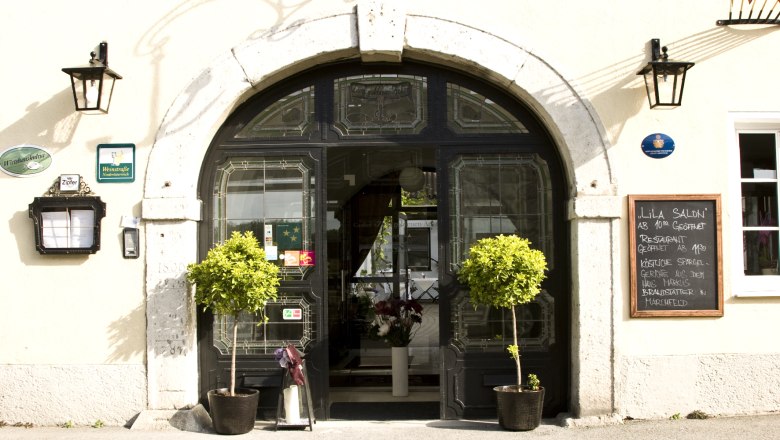 Hotel-Restaurant 'Zum goldenen Anker', © Hotel - Restaurant Zum goldenen Anker Eingang eines Restaurants mit dekorativen Pflanzen und einer Tafel mit Menüangeboten.