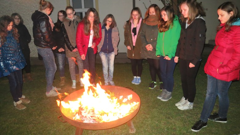 Feuerstelle, © K-Haus Gruppe von Jugendlichen steht um eine Feuerstelle im Freien.