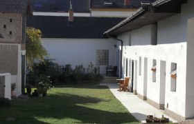 Wohlfühloase Edelmann, © Josef Edelmann Hof mit Rasenfläche, weißen Gebäuden und Gartenmöbeln.