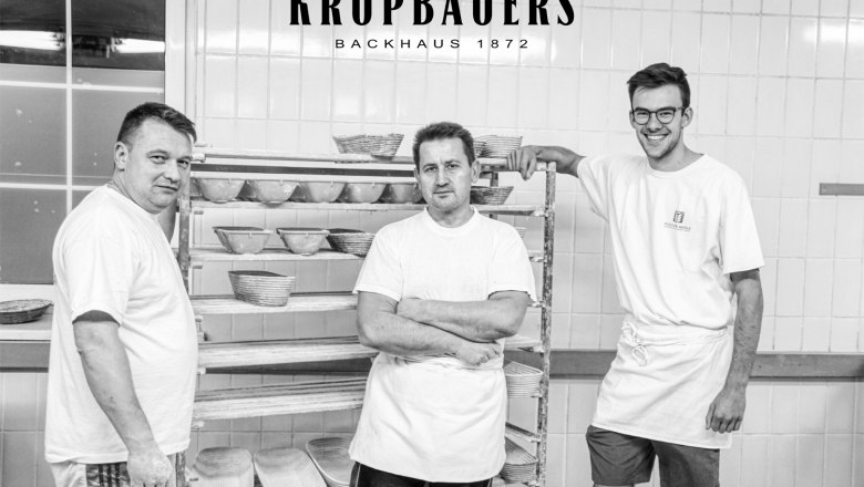 Backstube Krupbauers Backhaus 1872, Bruck/Leitha, © Krupbauers Backhaus 1872 Drei Bäcker in einer Backstube mit Brotkörben im Hintergrund.