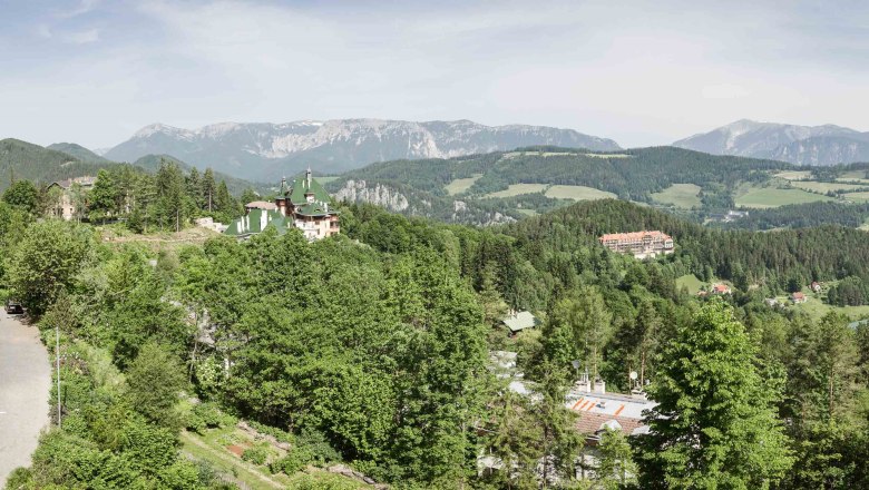 Aussicht vom Hotel, © Sebastian Freiler Panoramablick auf eine bergige Landschaft mit Wald, Straße und Gebäuden.