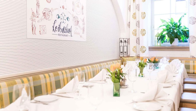 Innenräume im Loibnerhof, © Loibnerhof Elegantes Restaurantinterieur mit gedecktem Tisch, Blumen und Fenster mit Pflanze.