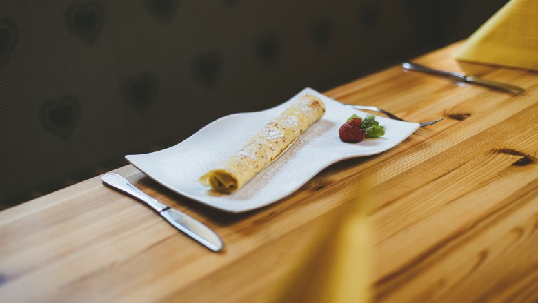 Süße Nachspeise: eine Palatschinke hat immer Platz im Bauch, © Niederösterreich Werbung/David Schreiber Eine Palatschinke auf einem weißen Teller mit Erdbeere und Minze, auf einem Holztisch serviert.