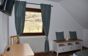 Aussicht aus dem Zimmer, © Familie König Innenansicht eines Zimmers mit Fenster, Tisch, Stuhl und Kommode.