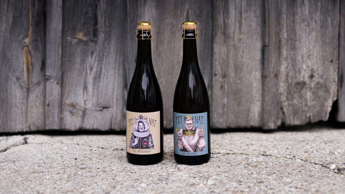 Apfel-Pet-Nats „Die Apfelkönigin“ und „Der Apfelkönig“, © Niederösterreich Werbung/Mara Hohla Flasche Apfel-Pet-Nats „Die Apfelkönigin“ und „Der Apfelkönig“ mit Karikaturen von Viktoria und Maximilian Preiß auf den Etiketten gestaltet von Künstlerin Linda Partaj
