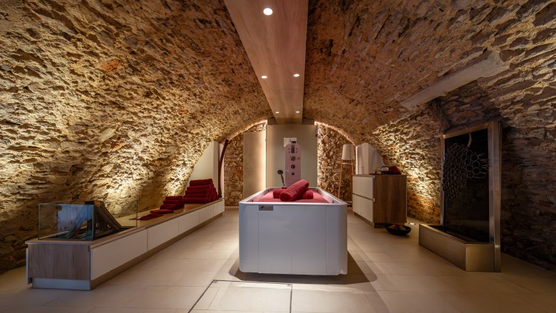 Landgut & SPA Althof Retz, © Niederösterreich Werbung / Maximilian Pawlikowsky Ein stilvoller Spa-Raum mit Steinwänden, einer modernen Badewanne und roten Handtüchern.