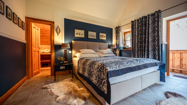 Forsthaus Langschlägerwald, © Niederösterreich Werbung / Maximilian Pawlikowsky Gemütliches Schlafzimmer mit Doppelbett, blauen Wänden und Holzelementen, angrenzend an eine Sauna.