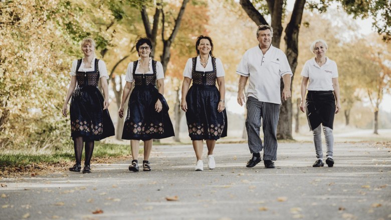 Das Wirtshaus-Team, © Niederösterreich Werbung/Rita Newman Fünf Personen in traditioneller Kleidung gehen auf einer von Bäumen gesäumten Straße.