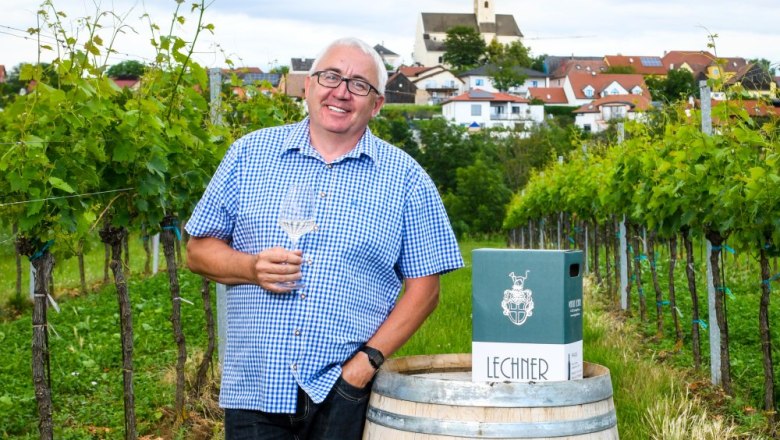 Reinhard Lechner, © zaiser@extra.krems.at Mann im karierten Hemd mit Weinglas in einem Weinberg, im Hintergrund ein Dorf mit Kirche.