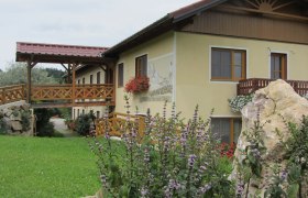Steinbauer, © Fam. König Ein gelbes Gebäude mit Holzbalkon und Blumen, umgeben von grüner Landschaft.