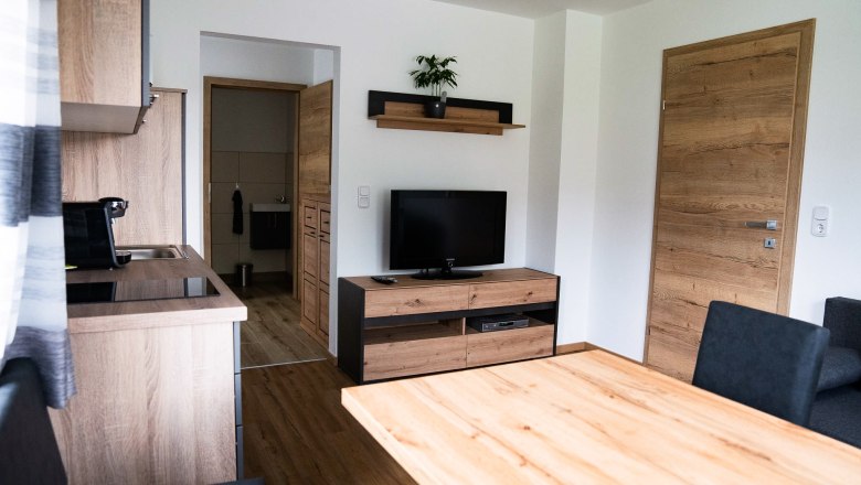 Wohn-/Esszimmer Richtung Schlafzimmer, © Manuel Hahn Modernes Wohnzimmer mit Holzmöbeln, Fernseher und Küche.