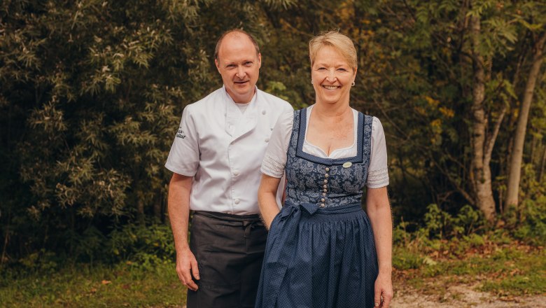 Wirtsleute Chefkoch Franz „Ferry“ Heinz & Gattin Gabi, © Niederösterreich Werbung/Daniela Führer Ein Mann in Kochuniform und eine Frau in traditioneller Tracht stehen lächelnd vor einem Wald.