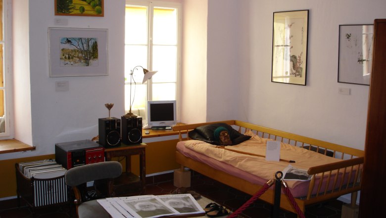 Gottfried von Einem Museum, © Stadtgemeinde Maissau Innenansicht eines Museumszimmers mit Bett, Bildern an der Wand und einem kleinen Schreibtisch mit Computer.