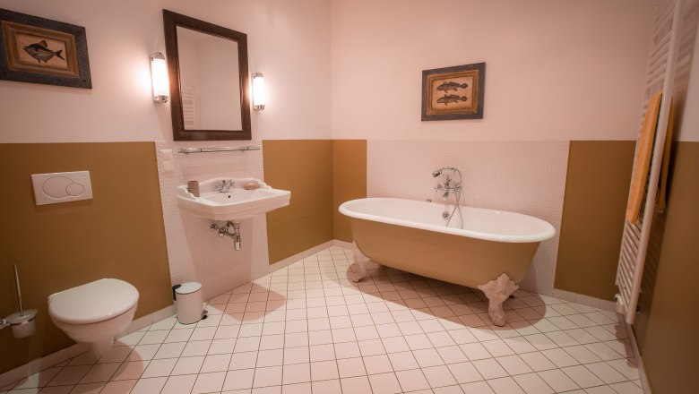 Bad - Doppelzimmer mit Schlossblick, © Schlossschenke Elegantes Badezimmer mit freistehender Badewanne, Waschbecken, Spiegel und WC. Wände in Beige und Weiß, dekoriert mit Fischbildern.